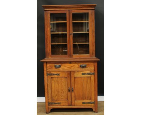 An Arts &amp; Crafts oak library bookcase, moulded outswept cornice above a pair of glazed doors enclosing adjustable shelves