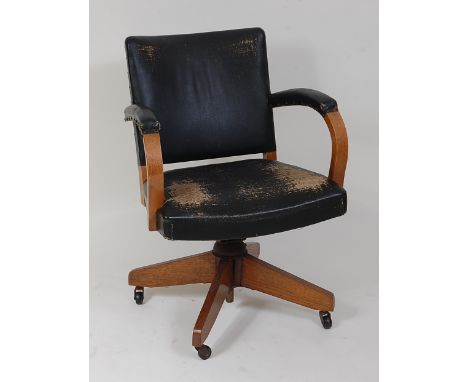 An Art Deco light oak swivel desk elbow chair, upholstered in black vinyl with studded detail, raised on roller castors, w.62