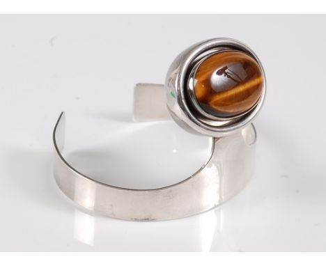 A silver and tigers eye bangle, the oval tigers eye cabochon, in collet mount with broad outer border, approx. 32mm wide, set