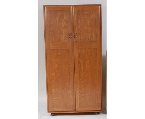 An Ercol blond elm double door wardrobe, having interior hanging rail, panelled back, and raised on roller castors, h.182.5cm