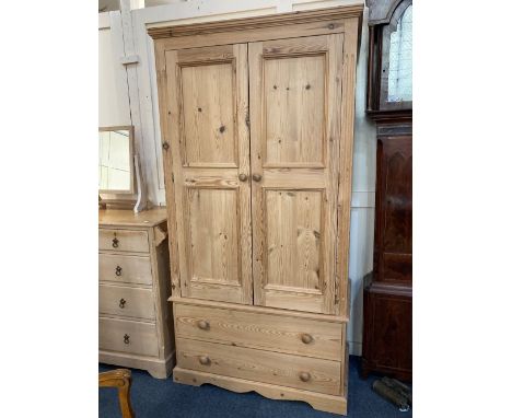 A pine wardrobe, with two panel doors enclosing a brass rail, and two drawers below, on bracket feet, 102cm 