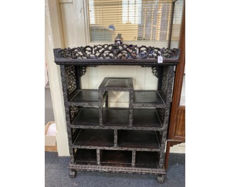 A Chinese carved hardwood display cabinet with pierced scroll gallery surmount above an arrangement of various shelves with p