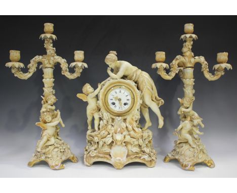 A Sitzendorf porcelain blush ivory clock garniture, late 19th/early 20th century, the clock surmounted by a semi-nude female 