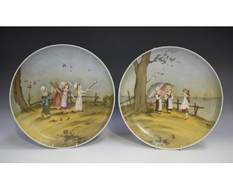 A pair of porcelain circular wall plates, each painted with Kate Greenaway style children, one depicting four young girls pla