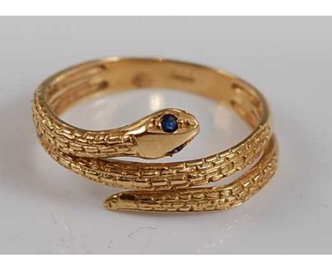 A yellow metal snake ring, the head set with two sapphires, the body engraved with a textured scale pattern halfway around, s