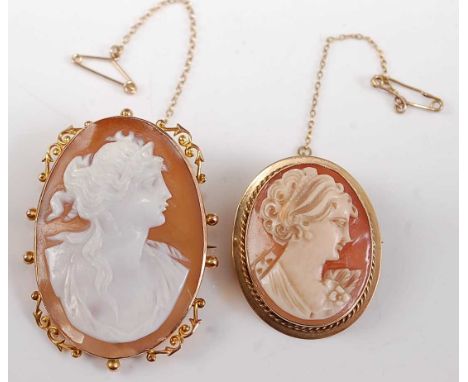 Two oval carved shell cameo brooches, one with a Roman woman in profile with a yellow scrollwork border, hook clasp and safet