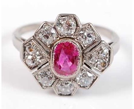 A white metal, ruby and diamond Art Deco style lozenge shaped cluster ring, featuring a centre oval ruby in a bezel setting, 