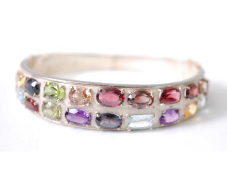 A white metal multi-stone oval hinged bangle, set with the following stones; two sapphires, total weight 3.07 carats; seven g