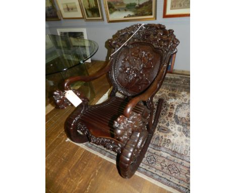 An unusual Chinese carved hardwood rocking chair, having a relief carved dragon cresting rail, above a panelled back relief c