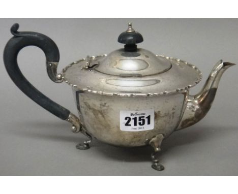 A silver teapot, of compressed circular form, having a decorated rim, raised on three pad feet, with black fittings, Birmingh
