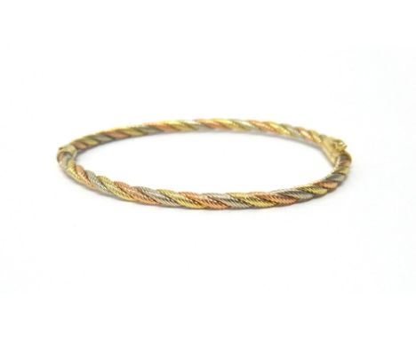 A three colour gold oval hinged bangle, in a ropetwist design, on a snap clasp, with a foldover safety catch, detailed 14 K, 
