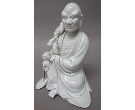 A Chinese blanc-de-chine figure of Li Tieguai, probably early 20th century, seated holding a bowl and rosary, hugging a staff