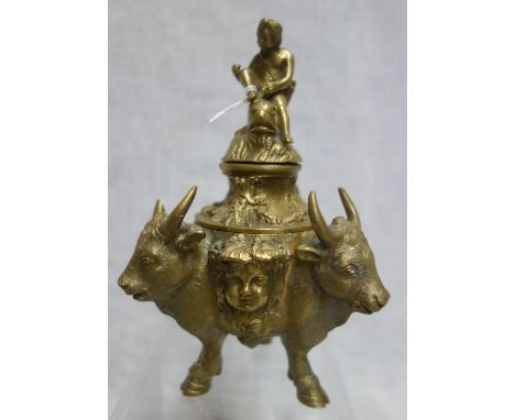 A 19TH CENTURY BRASS INKWELL, cast with three cattle heads, standing on three hooves with an Eros finial, 16.5cm high (overal