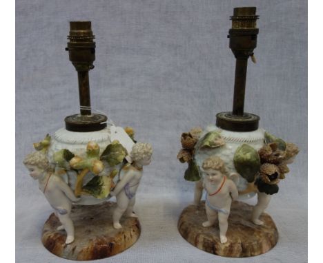 A PAIR OF CONTINENTAL CERAMIC OIL LAMPS supported by cherubs (with later electric fittings, not drilled)
