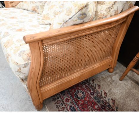 An Ercol ash and woven cane bergere three piece suite, two seater sofa and pair of armchairs, upholstered in Arts and Crafts 