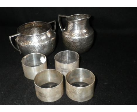 A planished silver cream jug and two handled sugar bowl and a set of four silver engine-turned napkin rings, some engraved wi