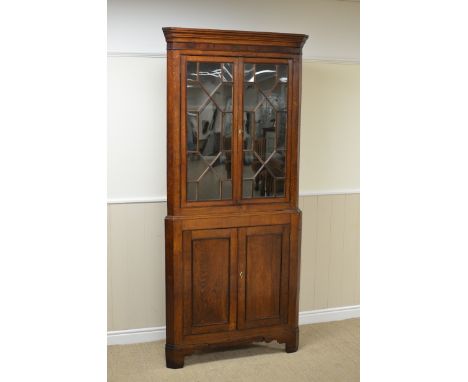 An early 19th Century oak Corner Cabinet, mahogany frieze above pair of astragal glazed doors enclosing shaped shelves, pair 