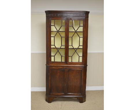 A Georgian oak Double Corner Cabinet with cross-banded frieze above a pair of astragal glazed doors, pair of solid panelled d