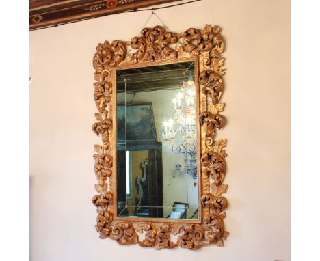 Gilded wood mirror Italy, 20th centuryrectangular frame richly carved with plant motifs and opposite scrolls220x145 cm.
