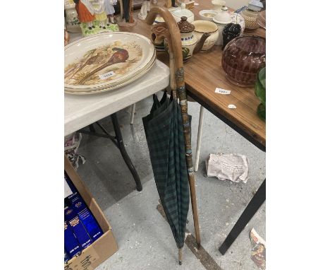 A VINTAGE GREEN TARTAN UMBRELLA WITH A FIGURE HEAD HANDLE PLUS A WALKING STICK WITH ATTACHED SOUVENIR BADGES 