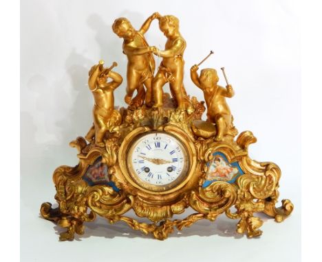 Late 19th century gilt metal mantel clock depicting putti playing instruments and dancing on rocky outcrop with rococo scroll