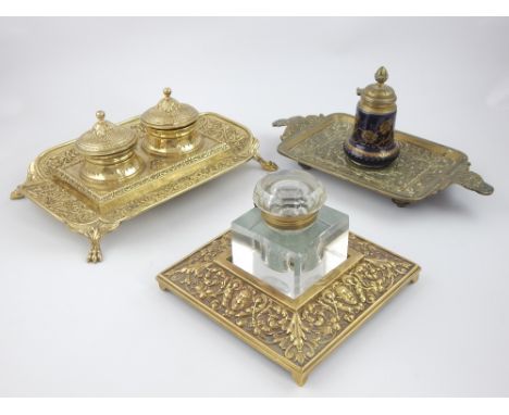 Three continental late 19th Century brass inkwells: desk top pieces, one with pan mask and foliate decoration and glass cube,