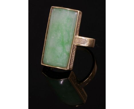 An 18ct gold jade ring,by Bernard Instone, with a rectangular curved jade plaque, rub set to a collet with hand engraved scro