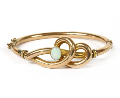 A gold opal set hollow hinged bangle, knot motif upper half rub set with an oval cabochon opal, to plain round section lower 