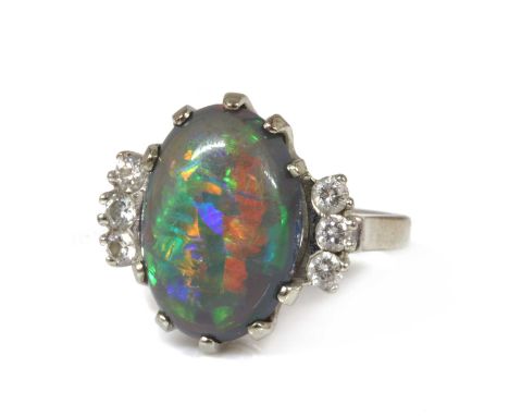 An American white gold black opal and diamond ring, an oval cabochon opal claw set to a rex collet with a pierced underbezel,