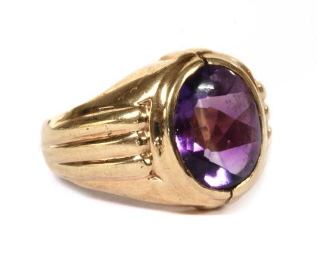 A gold single stone amethyst ring, an oval buff top amethyst, rub set, to ridged shoulders and a plain shank, tested as appro