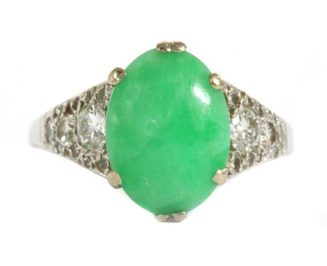 A white gold jade and diamond ring, an oval cabochon jadeite jade, 11.5 x 8.5 x 4.2mm, claw set to tapered shoulders, grain s