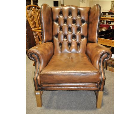 A modern brown leather button upholstered wing armchair.