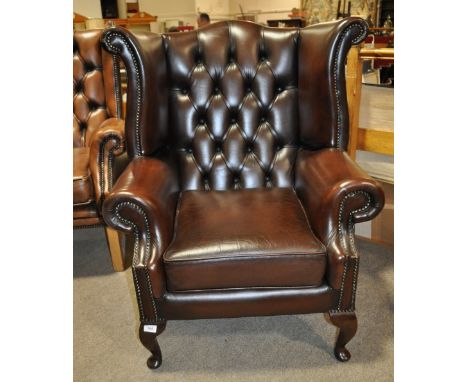 A modern dark brown button backed leather wing back armchair.