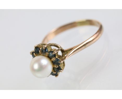 Gold pearl and blue stone ring. The ring being set with a pearl to cultured centre with a halo of round cut blue stones. Mark