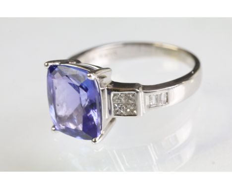 18ct gold tanzanite and diamond ring. The ring being set with a cushion cut tanzanite flanked 14 princess and step cut diamon