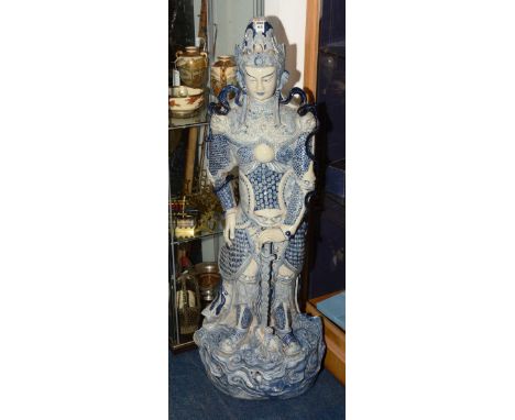 A large Eastern glazed pottery figure of a warrior, decorated with grotesque masks, on a blue and white ground, 123cm high. C