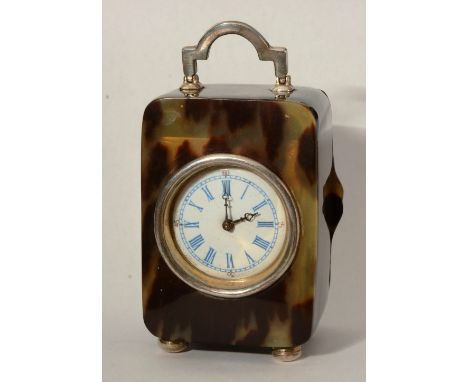 An early 20th century simulated tortoiseshell cased travel/desk clock, with silver carry handle above white enamel dial, rais