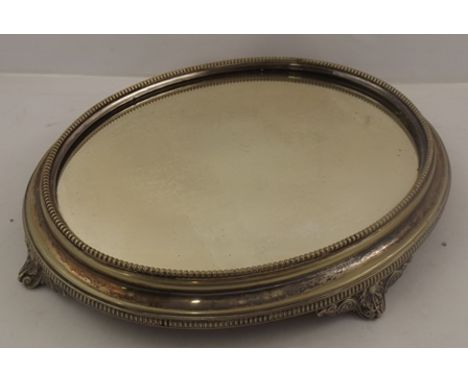 AN OVAL EPNS CAKE STAND, having mirror base, beaded surround, and raised on four cast scroll feet, 7.5cm x 46cm 