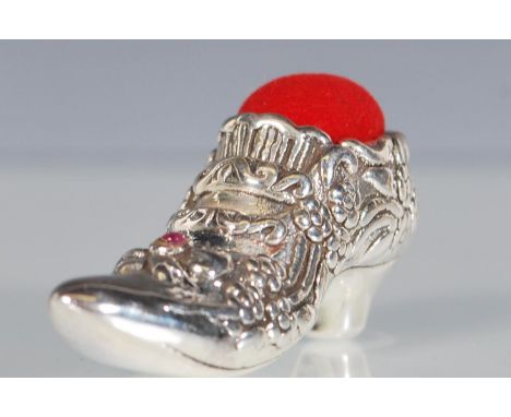 A Victorian style silver pin cushion in the form of a ladies shoe having floral decoration set with a single ruby cabochon wi