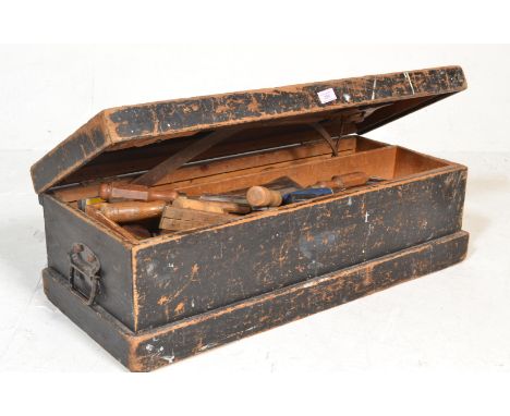 An early 20th Century carpenters ebonised wooden tool chest having twin swing handles, filled with a large selection of woodw