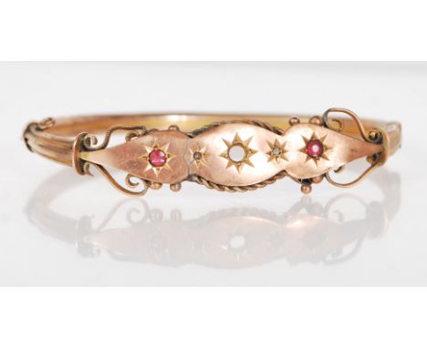 A late 19th Century Victorian 9ct gold bangle bracelet having two gypsy set red stones, with openwork scroll design and hinge