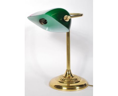A vintage 20th Century bankers desk lamp having an adjustable green glass shade raised on a brass support and repousse decora