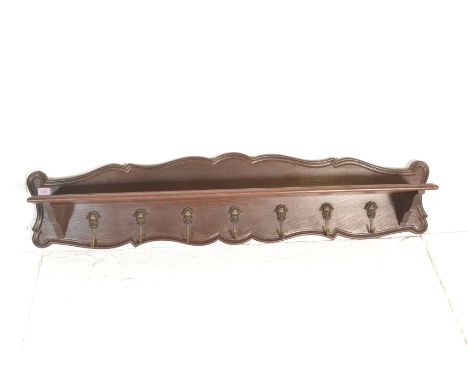 A 20th Century oak wall mounted coat rack of rectangular scroll form having a single shelf above seven brass mask coat hooks.