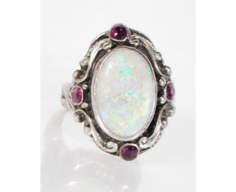 A 20th Century silver ring set with an oval opal panel and four red stones in a scrolled decoration mount. Unmarked. Weight 6