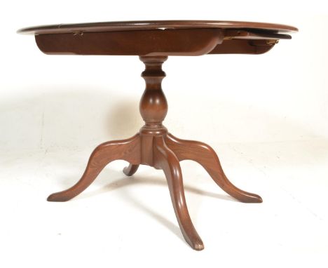 A 20th century Ercol beech and elm wood circular extending dining table being raised on a tripod base with extending circular