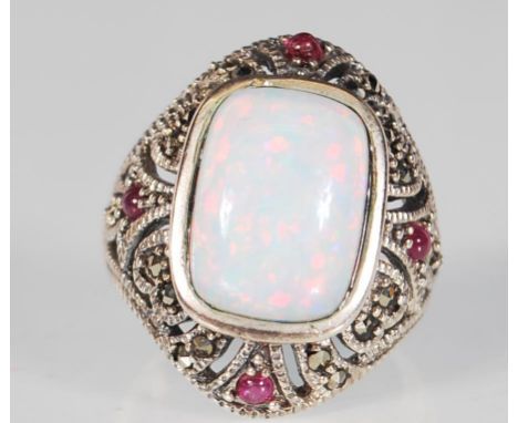 A silver and marcasite ring having a central opal panel on a decorative mount with red accent stones. Ring size O. Gross weig