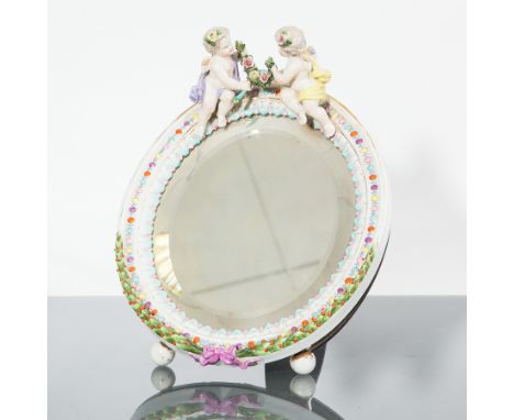 19TH CENTURY UPRIGHT BEVELLED TABLE MIRROR
contained in a ceramic frame of Meissen design, with an outset cresting of two che