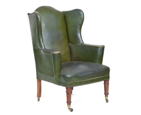 A late Victorian wingback armchair, upholstered in green leather, on ring turned legs with brass can ceramic casters, the sea