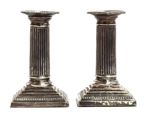 A pair of loaded silver neoclassical candlesticks by William Hutton &amp; Sons Ltd, London 1894, the reeded columns on square