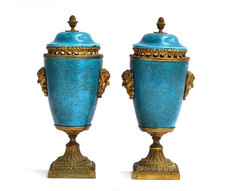 A pair of turquoise enamel and gilt metal lidded urns, with mask decoration and pierced collars, the lids surmounted with aco
